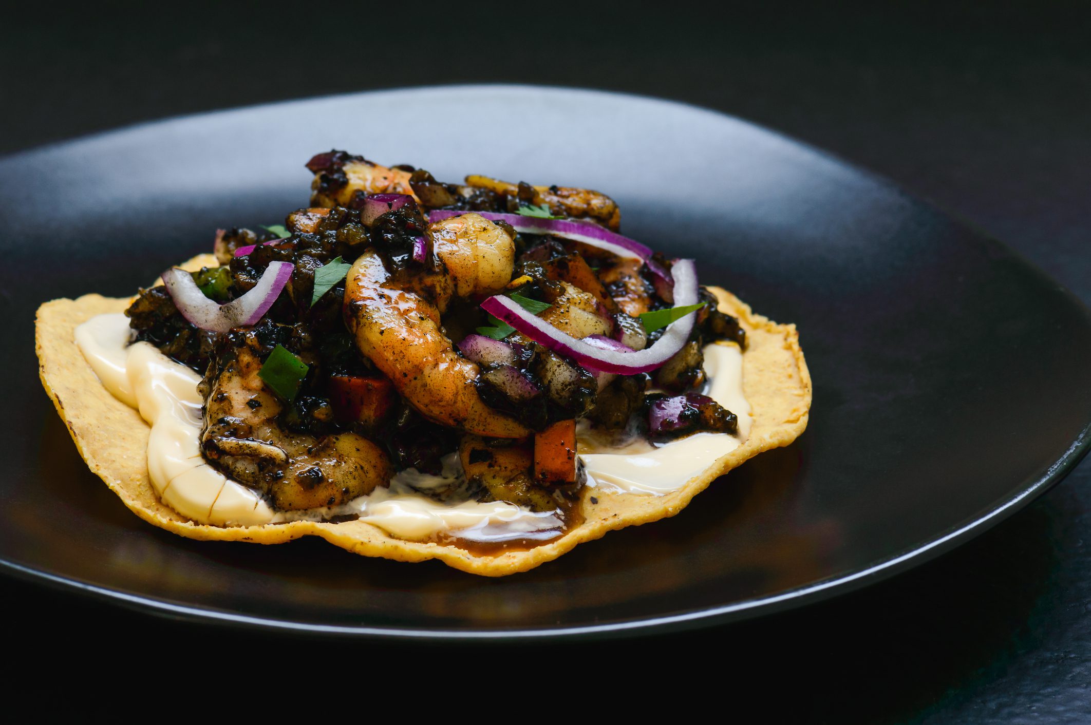 Shrimp and vegetables on tostada with sauce.