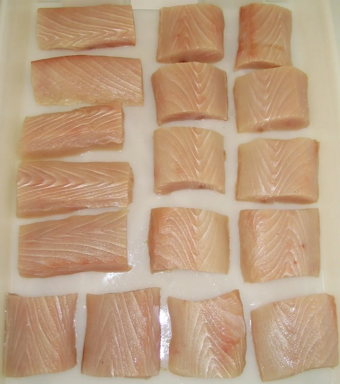 Sixteen raw fish fillets on a tray.
