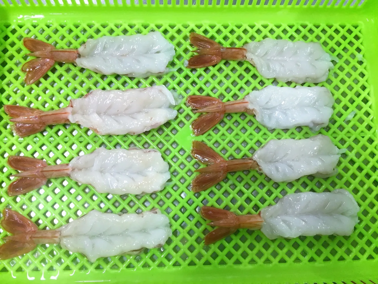 Eight peeled shrimp on a green tray.